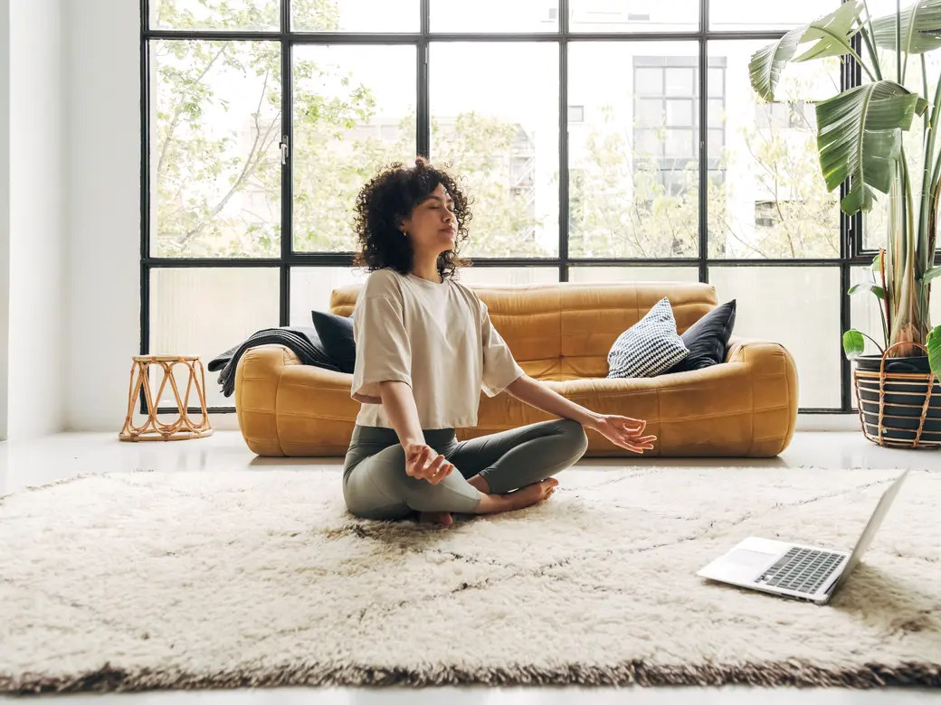 Frau, die zu Hause an Online-Video-Meditationsunterricht mit Laptop teilnimmt.