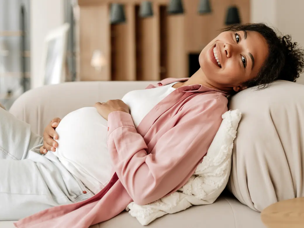 Schwangere Frau, die sich zu Hause auf dem Sofa entspannt und den Bauch berührt