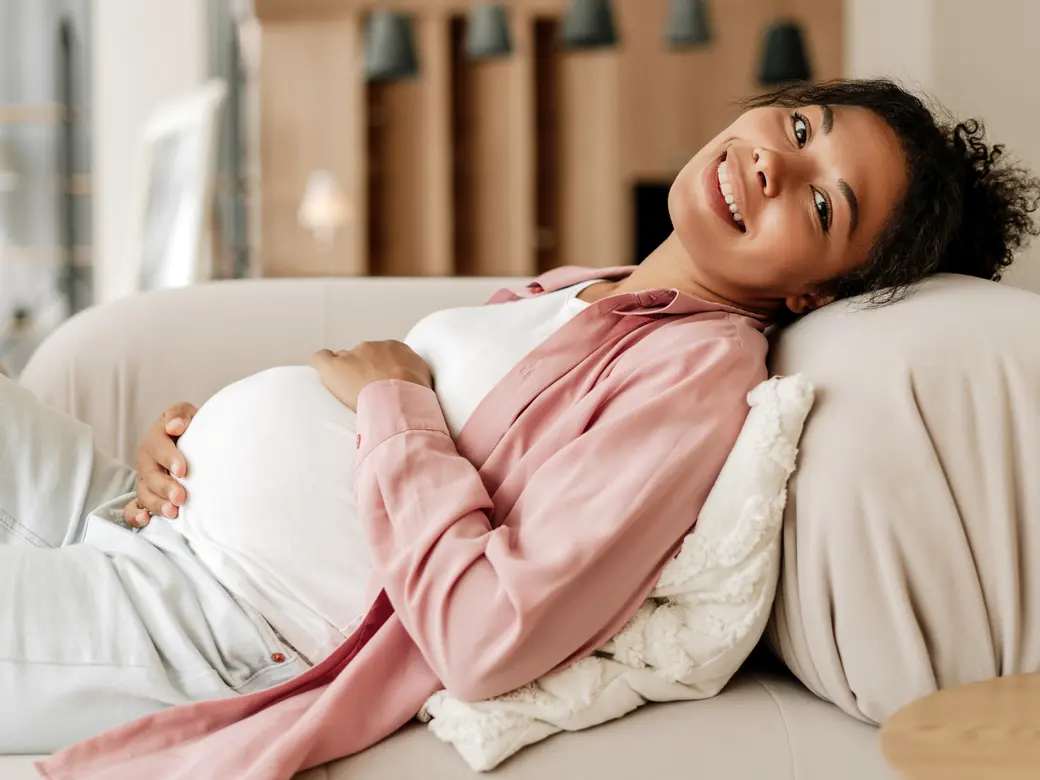 Schwangere Frau, die sich zu Hause auf dem Sofa entspannt und den Bauch berührt