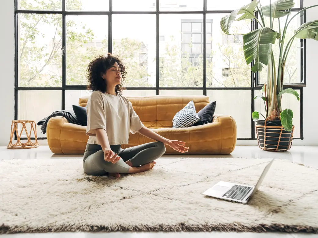 Junge Frau die zu Hause mit Online-Video-Meditationsunterricht mit Laptop meditiert