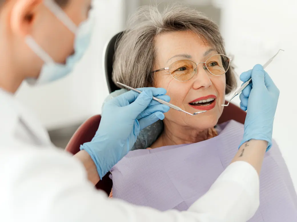 Seniorin, Patientin sitzt auf Zahnarztstuhl mit offenem Mund Arzt mit zahnärztlichem Instrumenten